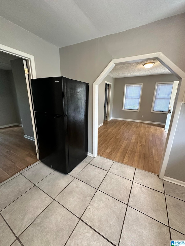 kitchen featuring black fridge, light wood-type flooring, and a textured ceiling