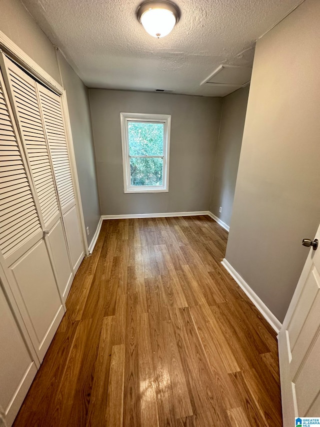 unfurnished bedroom with a textured ceiling, a closet, and hardwood / wood-style floors