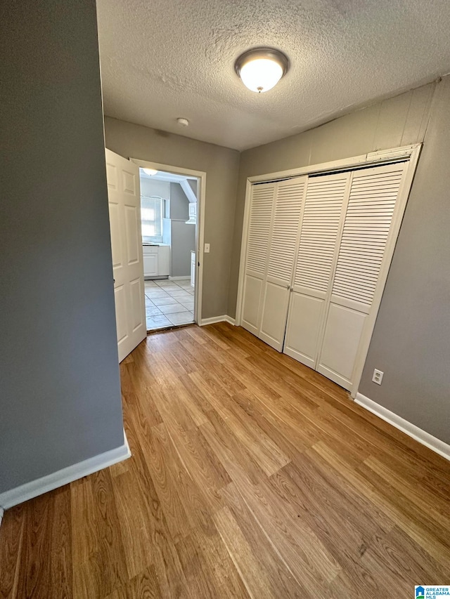 unfurnished bedroom with a textured ceiling, a closet, and light hardwood / wood-style floors