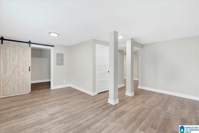 basement featuring a barn door, electric panel, and light hardwood / wood-style flooring