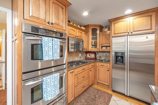 kitchen featuring backsplash, dark stone countertops, appliances with stainless steel finishes, and light tile patterned flooring