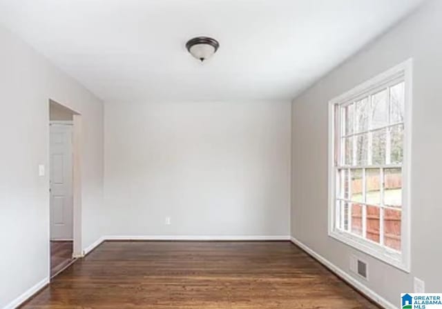 spare room with wood finished floors, visible vents, and baseboards