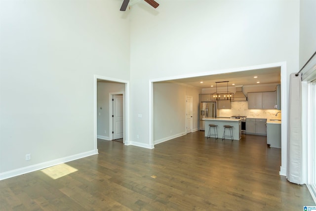 unfurnished living room featuring a towering ceiling, dark hardwood / wood-style flooring, and ceiling fan