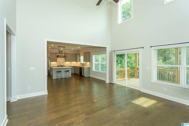 unfurnished living room with dark wood-type flooring, a healthy amount of sunlight, sink, and ceiling fan with notable chandelier