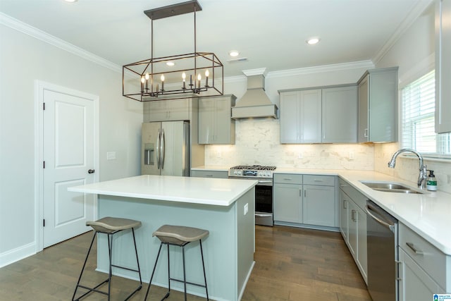 kitchen featuring appliances with stainless steel finishes, a notable chandelier, sink, premium range hood, and a kitchen island