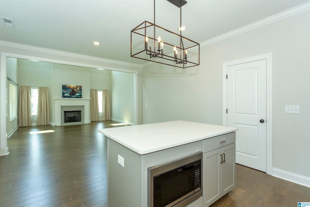 kitchen with dark hardwood / wood-style flooring, pendant lighting, crown molding, a center island, and stainless steel microwave