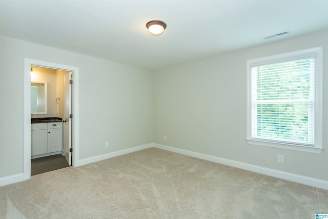 unfurnished bedroom featuring light carpet and ensuite bathroom