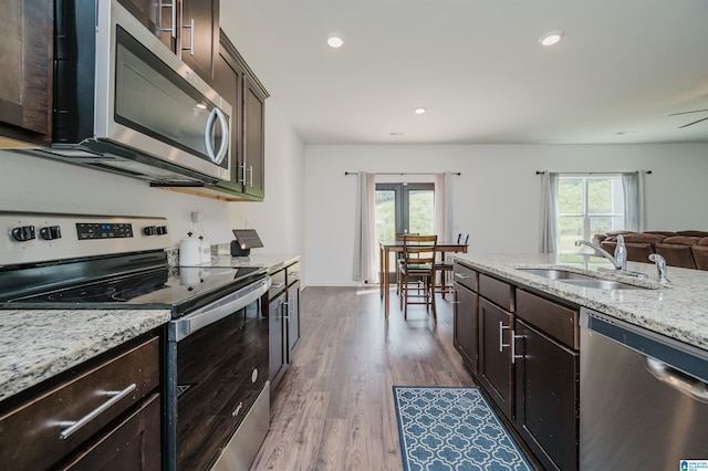 kitchen with hardwood / wood-style floors, appliances with stainless steel finishes, light stone countertops, sink, and dark brown cabinets