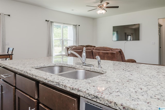 kitchen featuring ceiling fan, sink, light stone countertops, and dark brown cabinets