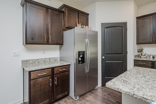 kitchen with stainless steel fridge with ice dispenser, dark brown cabinets, hardwood / wood-style flooring, and light stone countertops