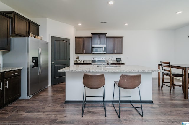 kitchen featuring a kitchen island with sink, dark wood-type flooring, light stone counters, and stainless steel appliances