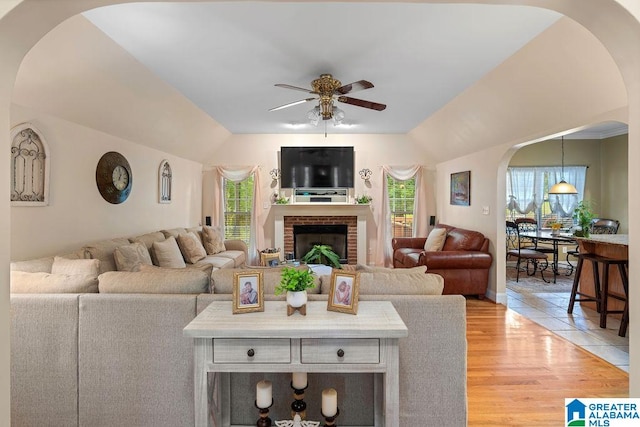 living room with ceiling fan, ornamental molding, light hardwood / wood-style floors, and a brick fireplace