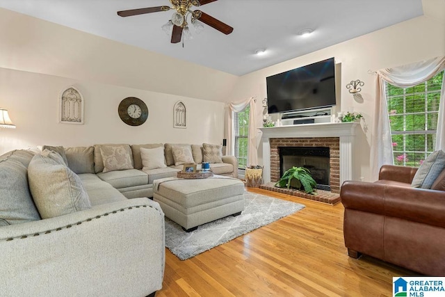 living area with a brick fireplace, ceiling fan, light wood finished floors, and vaulted ceiling