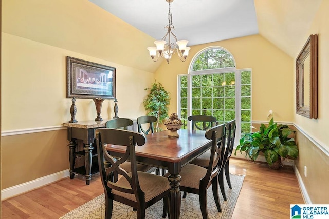 dining space with baseboards, a chandelier, lofted ceiling, and light wood-type flooring