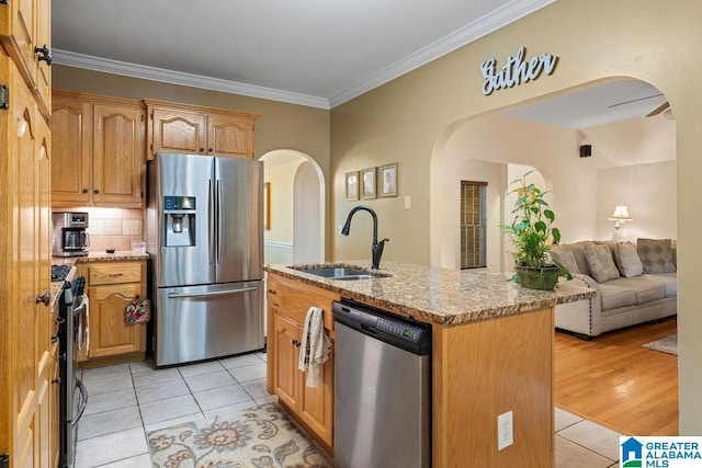 kitchen with light wood-type flooring, appliances with stainless steel finishes, sink, a kitchen island with sink, and ornamental molding