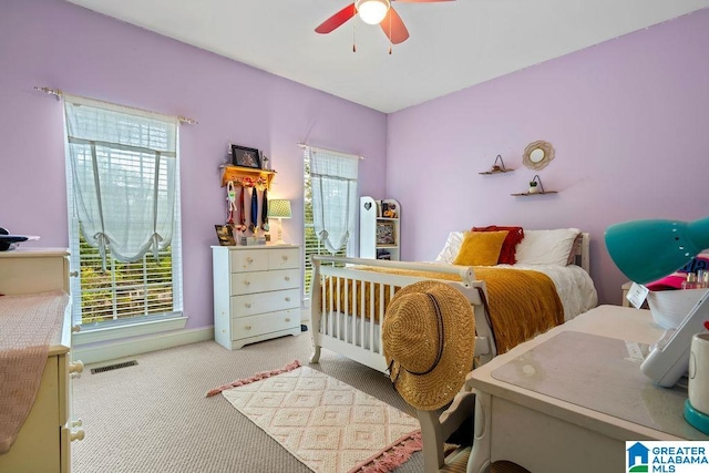 carpeted bedroom featuring ceiling fan, multiple windows, and a crib