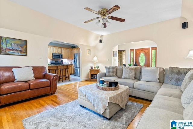 living room featuring arched walkways, ceiling fan, and light wood-style floors