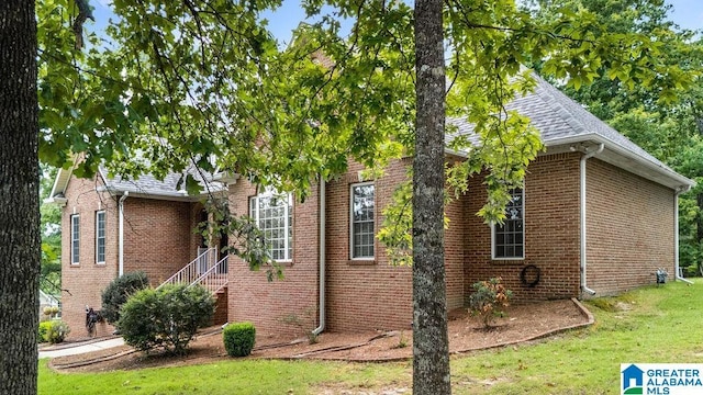 view of side of property with a lawn, a shingled roof, and brick siding