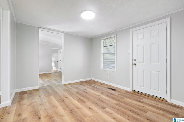 empty room with light wood-type flooring, a textured ceiling, and ornamental molding