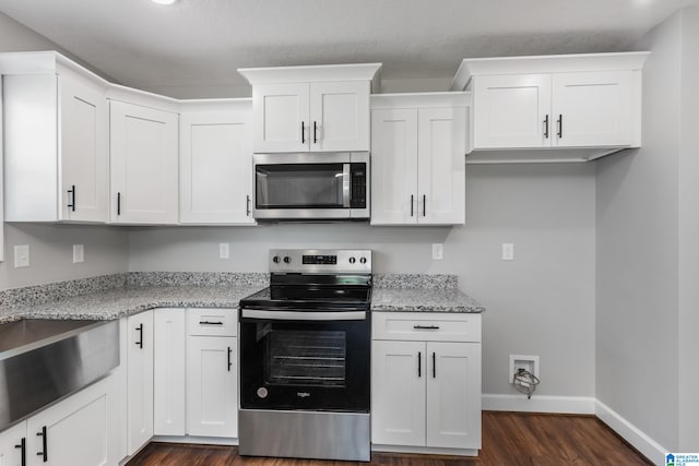 kitchen with appliances with stainless steel finishes, light stone countertops, dark hardwood / wood-style flooring, and white cabinetry