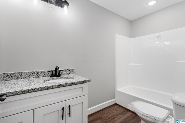bathroom with washtub / shower combination, vanity, toilet, baseboards, and wood finished floors