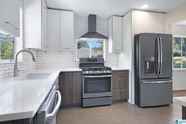 kitchen with stainless steel appliances, wall chimney range hood, white cabinets, and tasteful backsplash