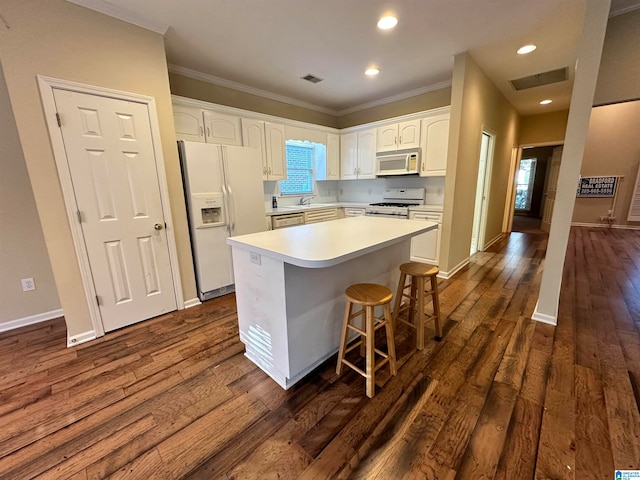 kitchen with white appliances, a center island, white cabinets, ornamental molding, and dark hardwood / wood-style floors