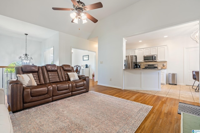 living room featuring light wood-type flooring, ceiling fan with notable chandelier, and lofted ceiling