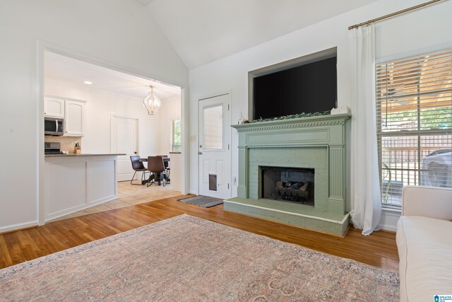 unfurnished living room featuring lofted ceiling, a fireplace, an inviting chandelier, and light hardwood / wood-style floors