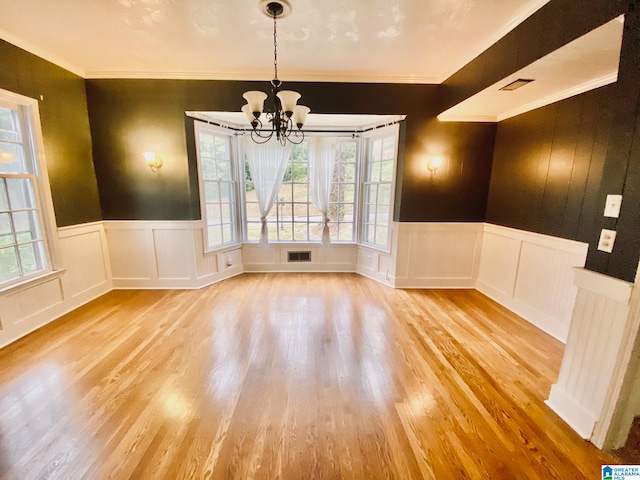 unfurnished dining area with a wealth of natural light, ornamental molding, a notable chandelier, and light wood-type flooring