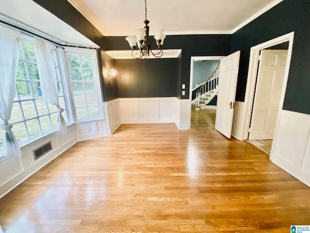 unfurnished dining area with crown molding, a notable chandelier, and light wood-type flooring