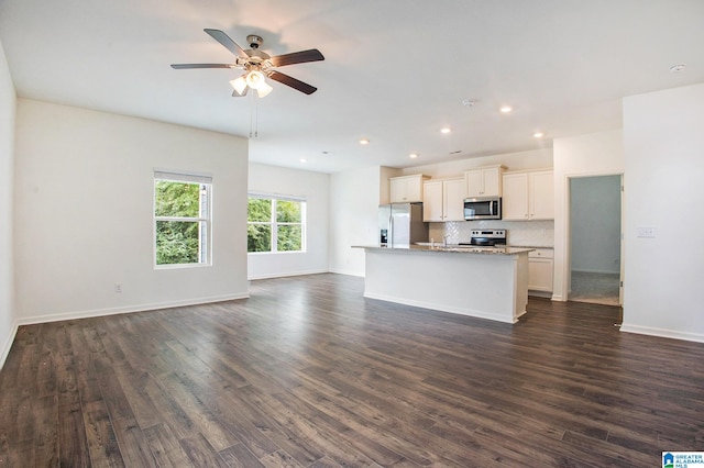 kitchen with light stone countertops, ceiling fan, dark wood-type flooring, appliances with stainless steel finishes, and a center island with sink