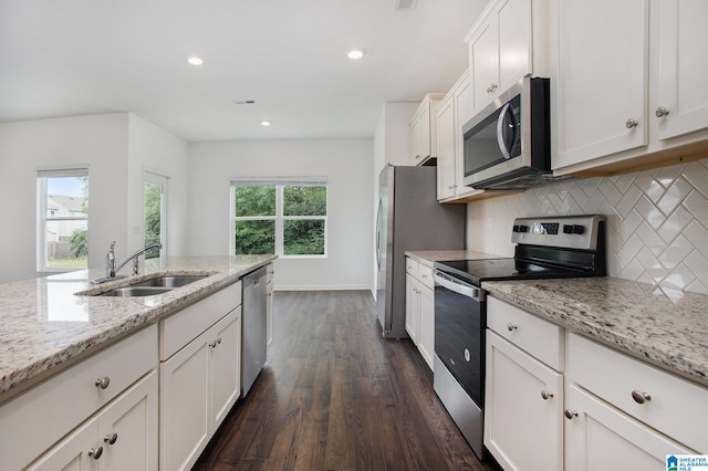 kitchen with appliances with stainless steel finishes, light stone countertops, white cabinetry, sink, and dark wood-type flooring