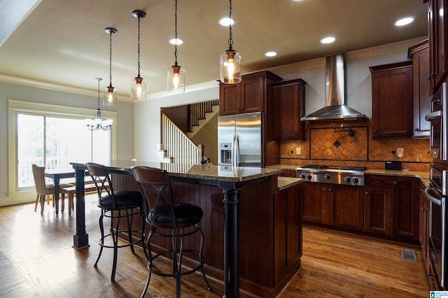 kitchen featuring appliances with stainless steel finishes, hardwood / wood-style flooring, dark stone countertops, and wall chimney range hood