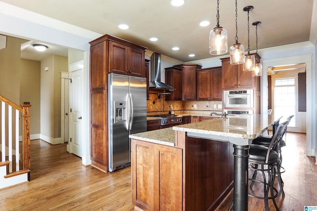 kitchen featuring a center island with sink, wall chimney range hood, light hardwood / wood-style flooring, appliances with stainless steel finishes, and light stone counters