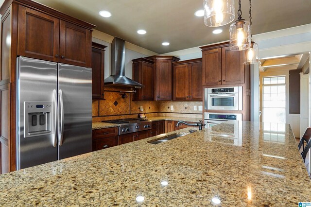 kitchen featuring light stone countertops, sink, wall chimney exhaust hood, hanging light fixtures, and stainless steel appliances