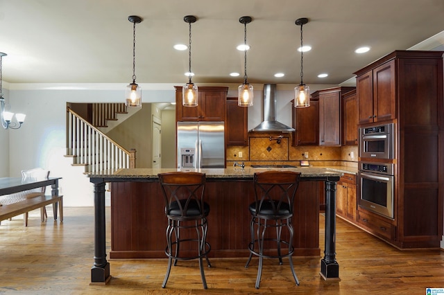 kitchen with a center island, wall chimney exhaust hood, stainless steel appliances, hardwood / wood-style floors, and decorative light fixtures