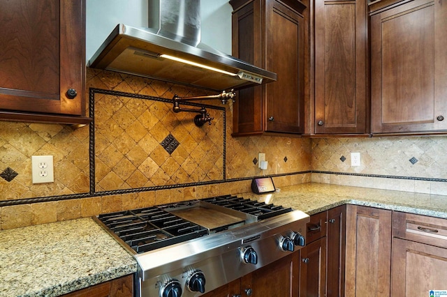 kitchen featuring backsplash, light stone counters, wall chimney exhaust hood, and stainless steel gas cooktop