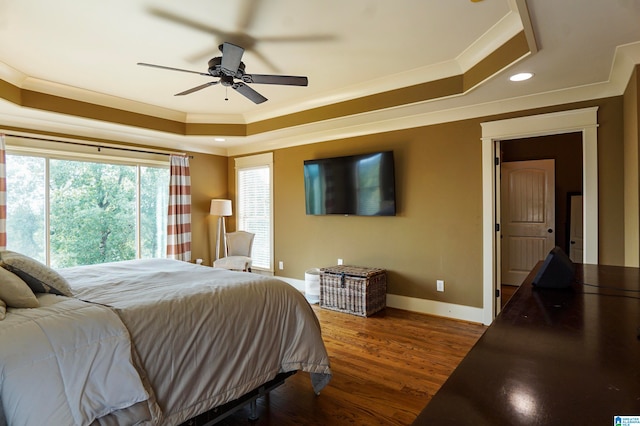 bedroom with ceiling fan, a raised ceiling, wood-type flooring, and ornamental molding