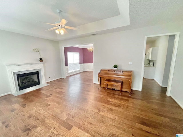 unfurnished living room with a textured ceiling, a premium fireplace, ceiling fan with notable chandelier, and light hardwood / wood-style floors