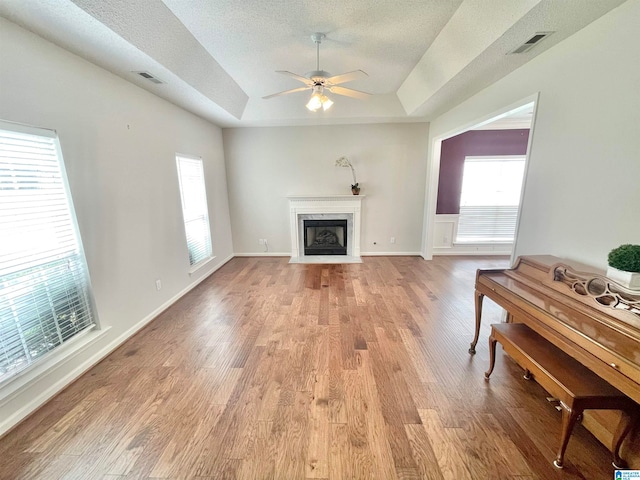 living room with light wood-type flooring, ceiling fan, a raised ceiling, and a textured ceiling