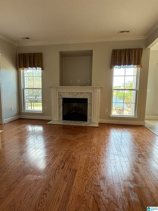 unfurnished living room featuring hardwood / wood-style floors, a wealth of natural light, crown molding, and a high end fireplace