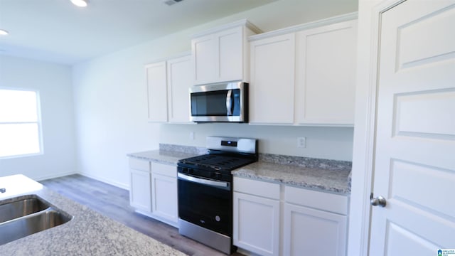 kitchen featuring sink, white cabinetry, light stone counters, wood-type flooring, and appliances with stainless steel finishes