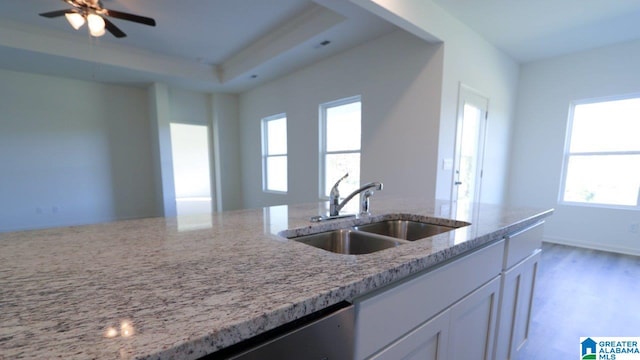 kitchen featuring sink, white cabinetry, a raised ceiling, ceiling fan, and light stone countertops