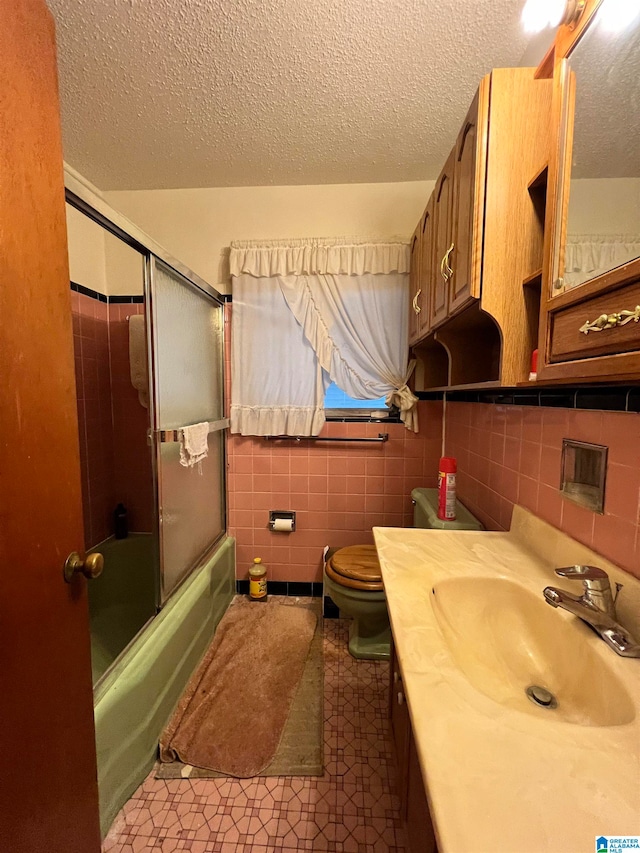 full bathroom with toilet, tile walls, vanity, bath / shower combo with glass door, and a textured ceiling