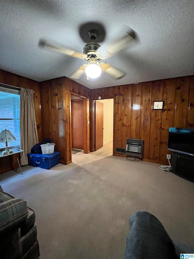 carpeted living room featuring wood walls, ceiling fan, heating unit, and a textured ceiling