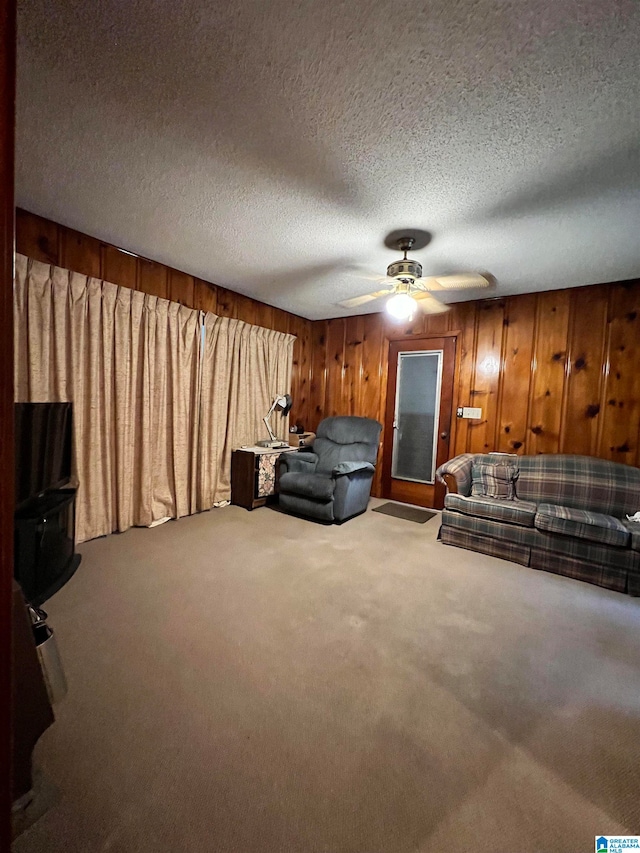 unfurnished living room with ceiling fan, wooden walls, carpet, and a textured ceiling