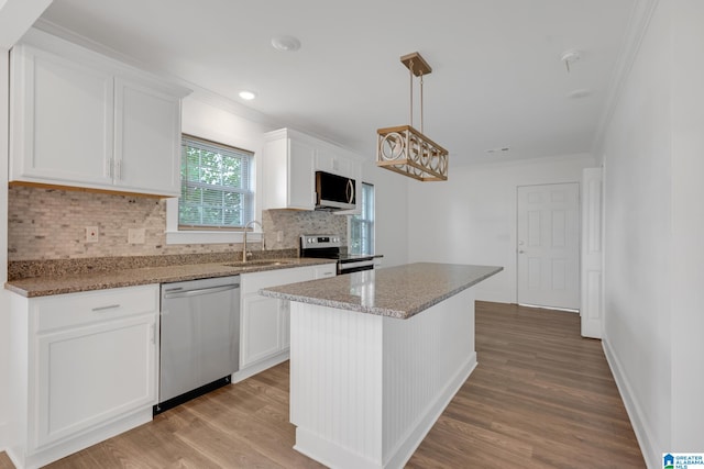 kitchen with stainless steel appliances, light stone counters, a center island, white cabinets, and light hardwood / wood-style floors