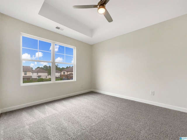 carpeted empty room with ceiling fan and a raised ceiling