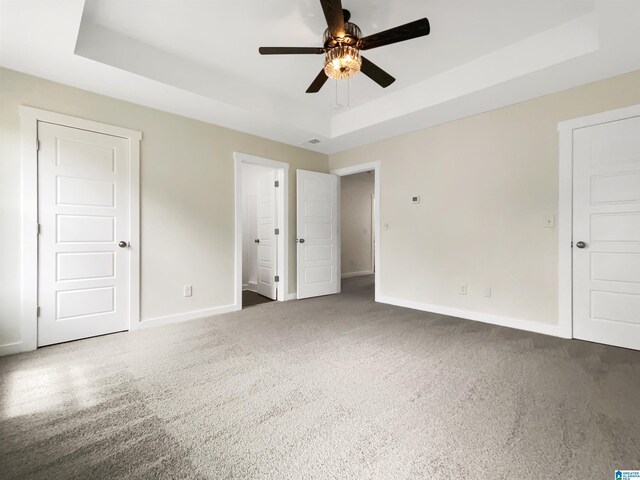 unfurnished bedroom featuring a raised ceiling, ceiling fan, and carpet